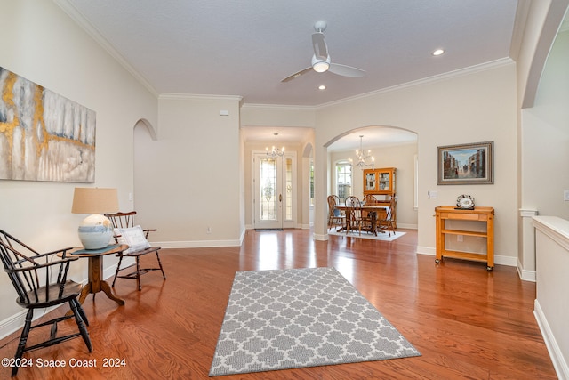 sitting room with ceiling fan with notable chandelier, wood-type flooring, and ornamental molding