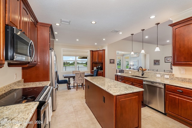 kitchen with appliances with stainless steel finishes, hanging light fixtures, a kitchen island, light stone countertops, and sink