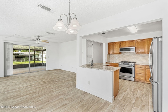 kitchen with hanging light fixtures, stainless steel appliances, light hardwood / wood-style floors, a textured ceiling, and ceiling fan with notable chandelier