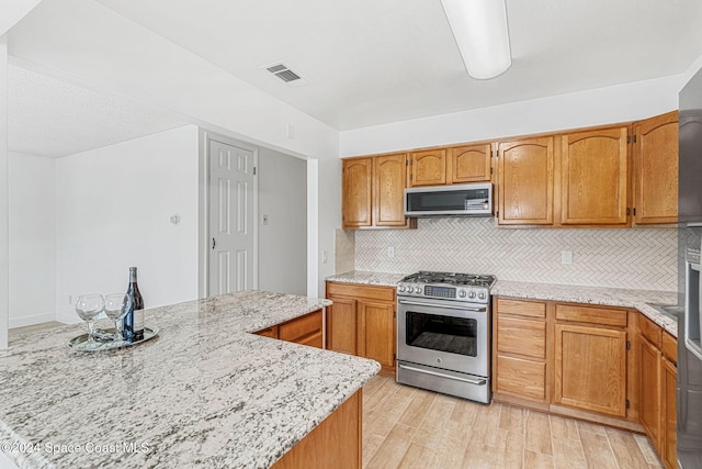 kitchen featuring light stone countertops, appliances with stainless steel finishes, light wood-type flooring, and tasteful backsplash