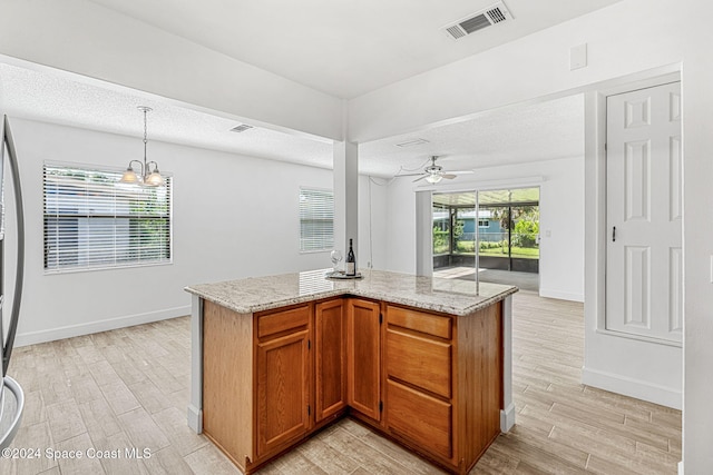 kitchen with light stone counters, ceiling fan with notable chandelier, a center island, light hardwood / wood-style floors, and hanging light fixtures