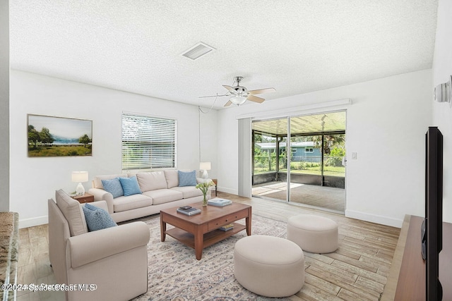 living room with a textured ceiling, light wood-type flooring, and ceiling fan