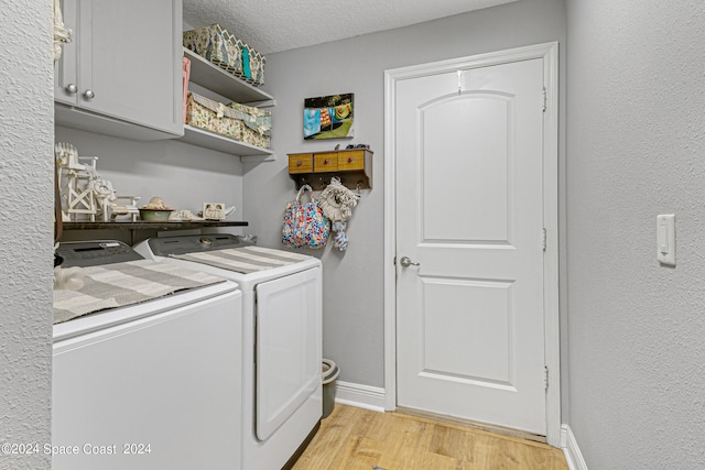 laundry area featuring light wood-type flooring, washer and clothes dryer, a textured ceiling, and cabinets