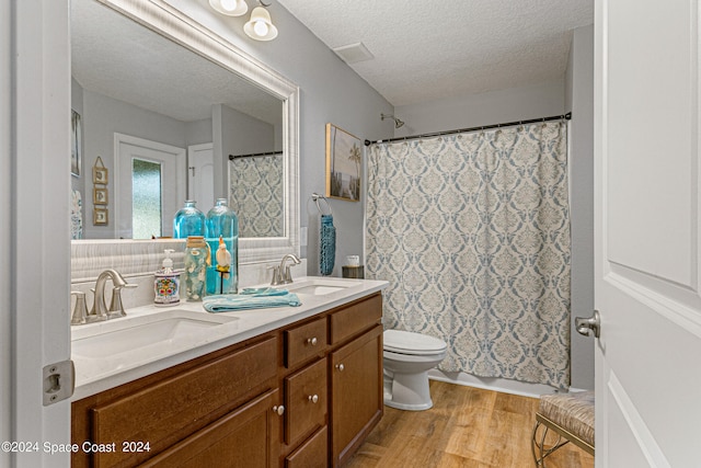 bathroom with a textured ceiling, walk in shower, hardwood / wood-style floors, vanity, and toilet