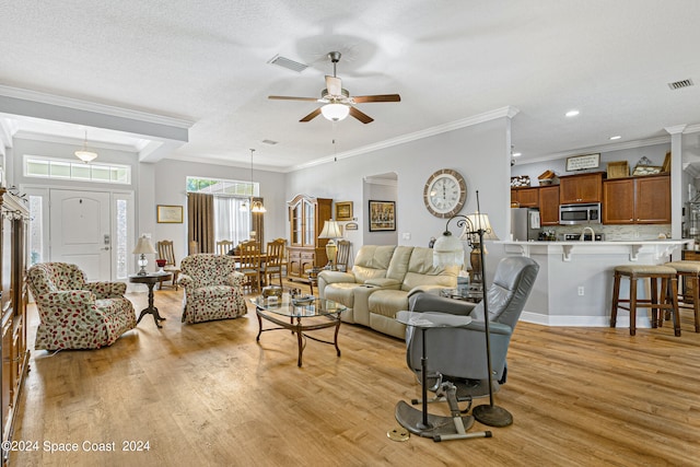 living room with light hardwood / wood-style flooring, a textured ceiling, ceiling fan with notable chandelier, and ornamental molding