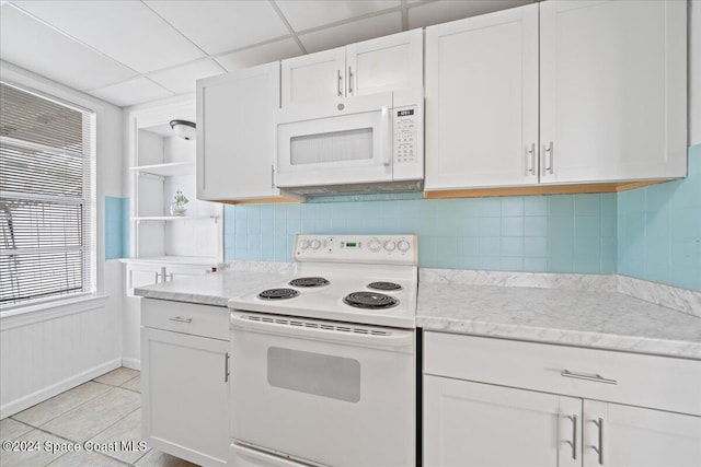 kitchen featuring a paneled ceiling, white cabinets, light tile patterned floors, and white appliances