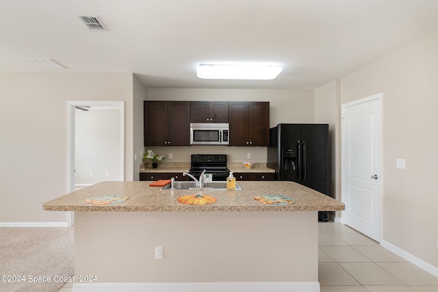 kitchen with dark brown cabinets, a center island with sink, sink, black appliances, and light tile patterned floors