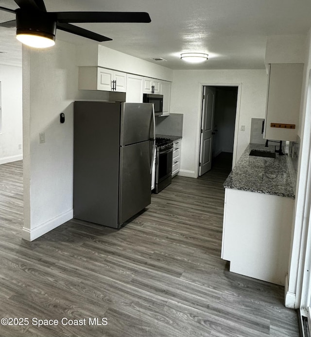 kitchen with gas stove, white cabinetry, dark stone counters, sink, and stainless steel refrigerator