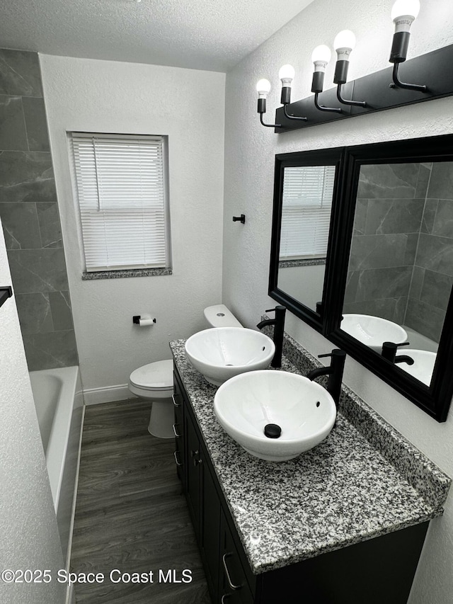 full bathroom with tiled shower / bath, hardwood / wood-style floors, a textured ceiling, toilet, and vanity