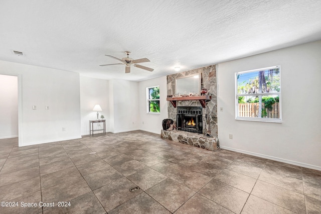 unfurnished living room with ceiling fan, a stone fireplace, and a textured ceiling