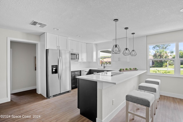 kitchen with light wood-type flooring, a textured ceiling, white cabinetry, kitchen peninsula, and appliances with stainless steel finishes