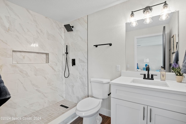 bathroom with a tile shower, a textured ceiling, hardwood / wood-style flooring, vanity, and toilet