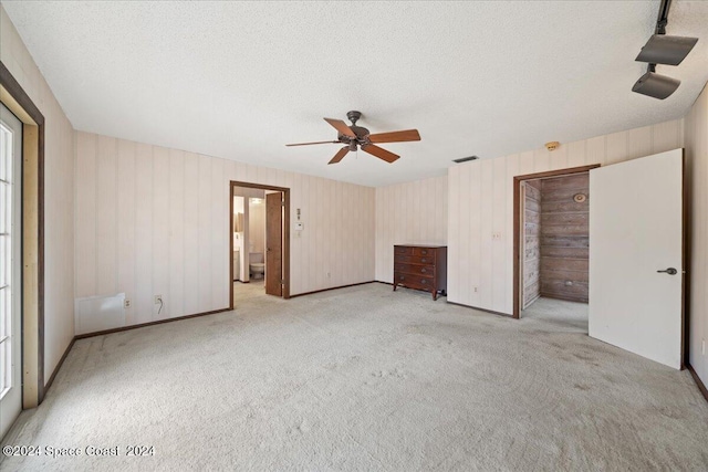 unfurnished bedroom featuring ceiling fan, light colored carpet, a textured ceiling, and ensuite bath