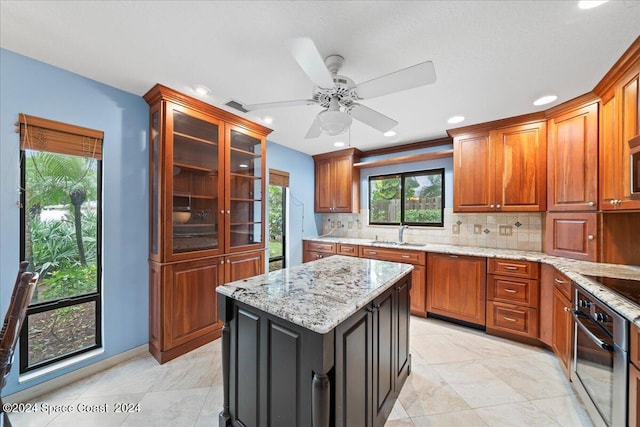 kitchen with sink, stainless steel oven, a center island, light stone countertops, and decorative backsplash