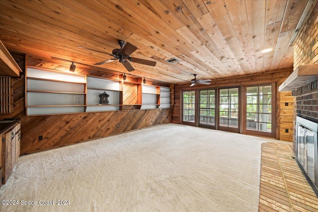 unfurnished living room with ceiling fan, a brick fireplace, wooden walls, wooden ceiling, and light carpet