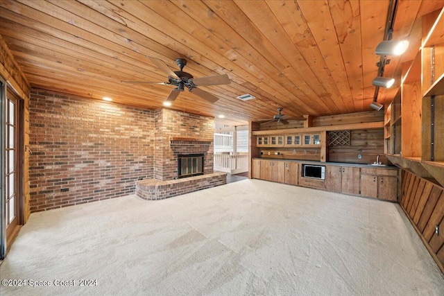 unfurnished living room featuring wooden ceiling, light colored carpet, brick wall, wooden walls, and a fireplace