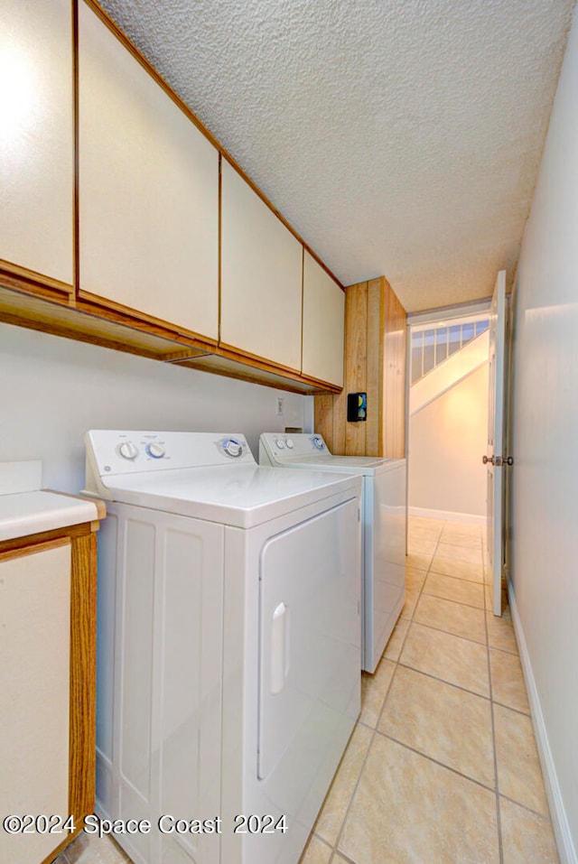 laundry room featuring cabinets, a textured ceiling, independent washer and dryer, and light tile patterned floors