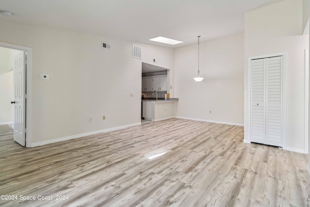 unfurnished living room with a skylight, light hardwood / wood-style flooring, and sink