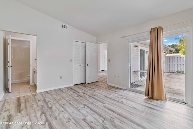 unfurnished bedroom featuring a closet, lofted ceiling, access to outside, light hardwood / wood-style flooring, and connected bathroom