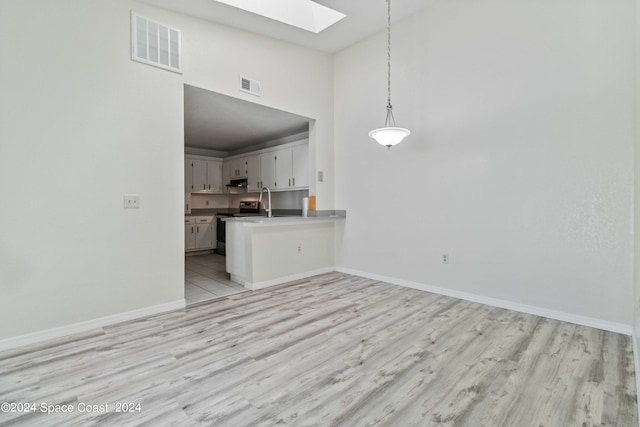 kitchen with white cabinets, kitchen peninsula, light hardwood / wood-style flooring, a towering ceiling, and a skylight