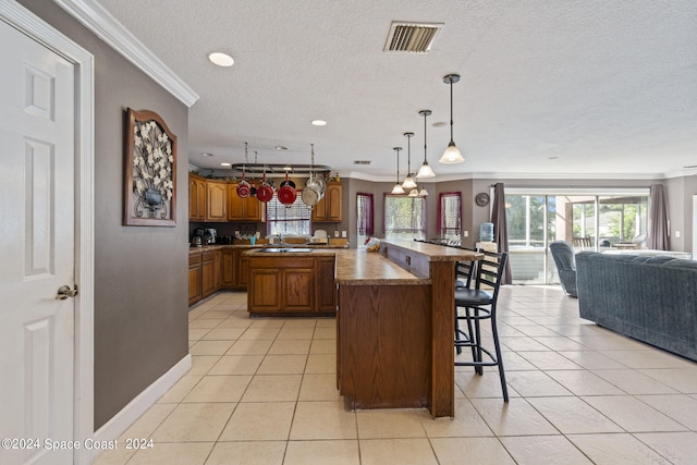 kitchen featuring hanging light fixtures, light tile patterned flooring, a breakfast bar area, crown molding, and a center island