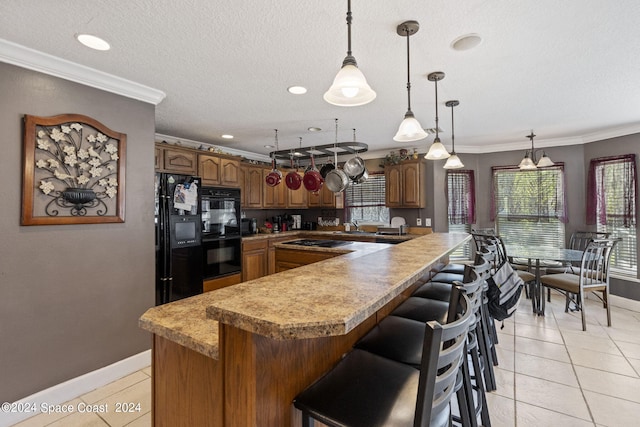 kitchen with pendant lighting, ornamental molding, kitchen peninsula, black appliances, and a breakfast bar area