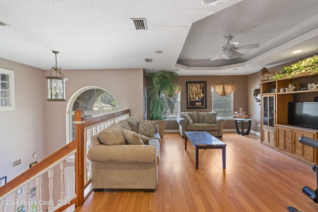 living room featuring a tray ceiling, light hardwood / wood-style floors, ceiling fan, and a textured ceiling