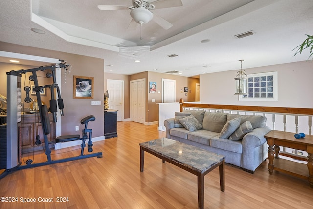 living room featuring a textured ceiling, a raised ceiling, ceiling fan, and light hardwood / wood-style flooring