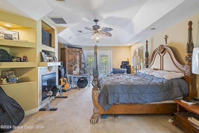 carpeted bedroom with ceiling fan, a textured ceiling, a tray ceiling, and a high end fireplace