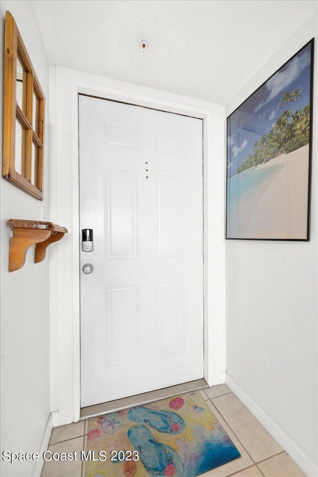 doorway with a textured ceiling and light tile patterned flooring