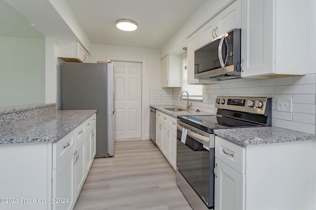 kitchen with light hardwood / wood-style floors, white cabinetry, light stone counters, stainless steel appliances, and sink