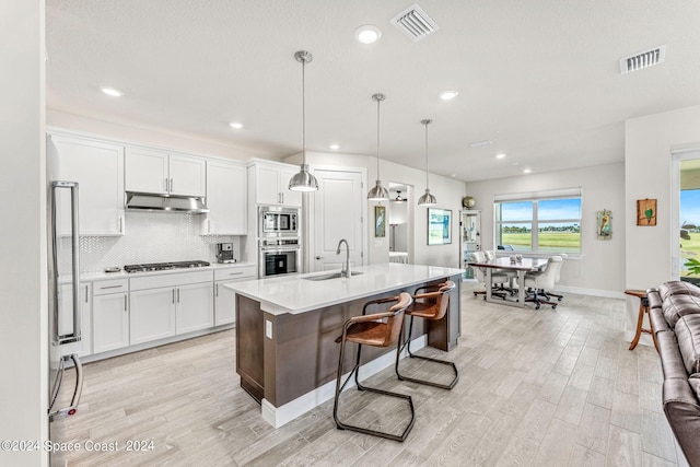 kitchen with white cabinetry, a center island with sink, appliances with stainless steel finishes, and decorative light fixtures