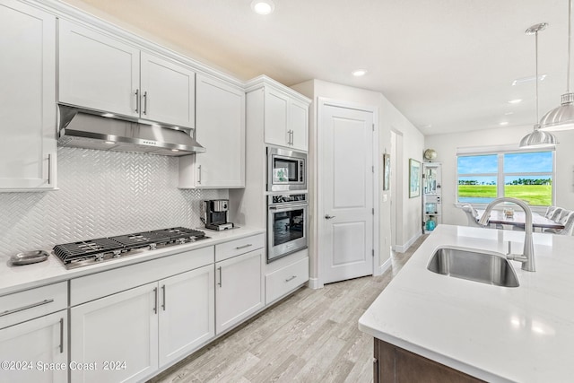 kitchen with light wood-type flooring, white cabinets, backsplash, appliances with stainless steel finishes, and decorative light fixtures