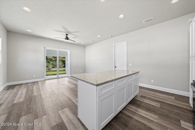 kitchen with light stone countertops, light wood-type flooring, a textured ceiling, a kitchen island, and white cabinetry