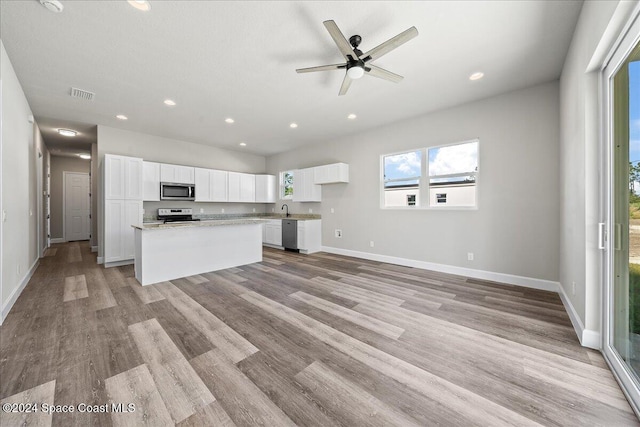 kitchen with light stone countertops, white cabinets, light hardwood / wood-style floors, a kitchen island, and appliances with stainless steel finishes