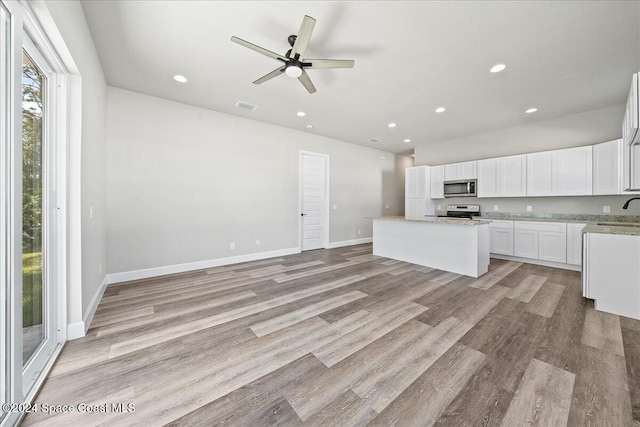 kitchen featuring light stone countertops, a center island, light hardwood / wood-style floors, white cabinets, and appliances with stainless steel finishes