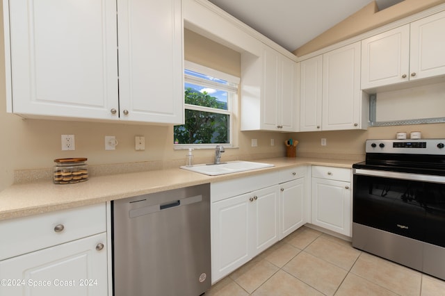 kitchen with vaulted ceiling, white cabinets, light tile patterned floors, stainless steel appliances, and sink