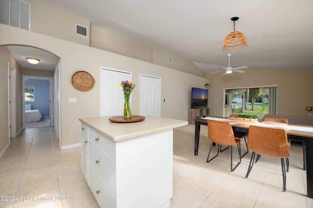 kitchen with white cabinets, lofted ceiling, a kitchen island, light tile patterned floors, and decorative light fixtures