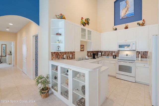 kitchen with a towering ceiling, backsplash, white appliances, and white cabinetry