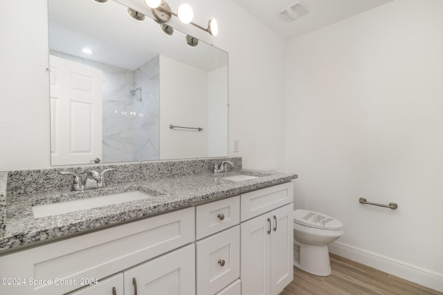 bathroom with wood-type flooring, tiled shower, vanity, and toilet