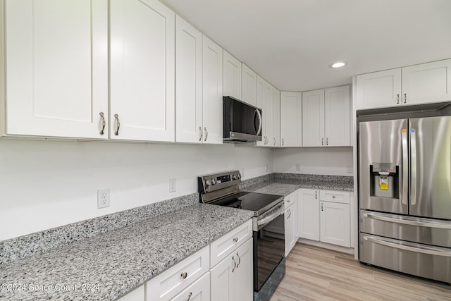 kitchen with light stone countertops, light wood-type flooring, white cabinetry, and appliances with stainless steel finishes