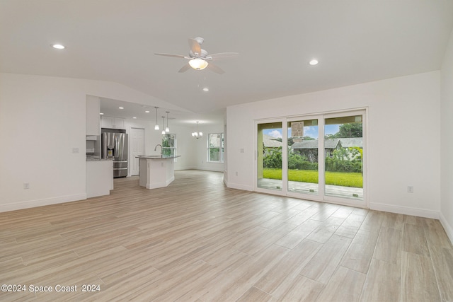 unfurnished living room featuring light wood-type flooring, ceiling fan with notable chandelier, and vaulted ceiling