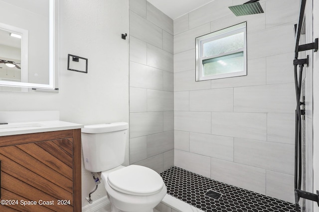 bathroom with ceiling fan, vanity, toilet, and tiled shower