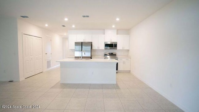 kitchen with a kitchen island with sink, white cabinetry, stainless steel appliances, backsplash, and light tile patterned floors