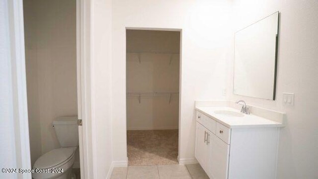 bathroom featuring vanity, baseboards, tile patterned floors, toilet, and a walk in closet