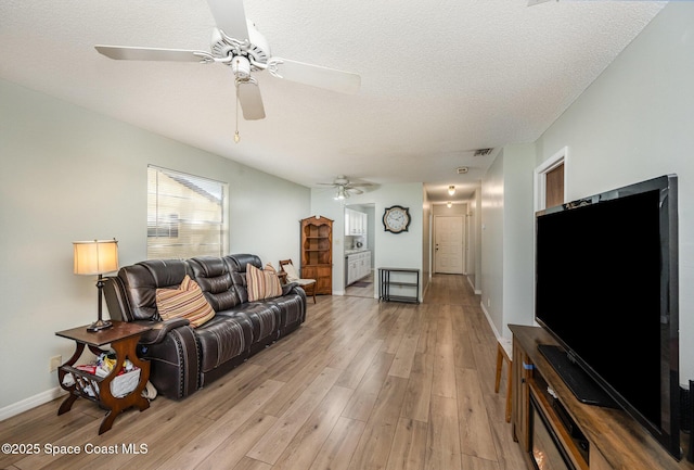 living area featuring visible vents, a textured ceiling, light wood-style floors, baseboards, and ceiling fan