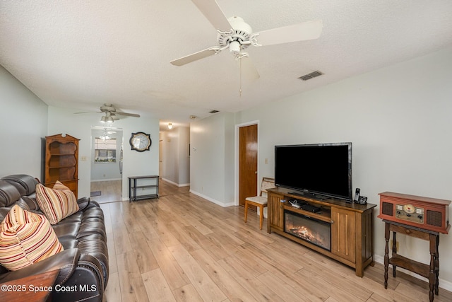 living room featuring visible vents, a ceiling fan, a textured ceiling, light wood finished floors, and baseboards