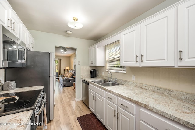 kitchen with light wood-type flooring, a sink, backsplash, white cabinetry, and stainless steel appliances