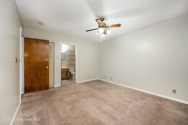 unfurnished bedroom featuring baseboards, light carpet, a textured ceiling, and ensuite bathroom