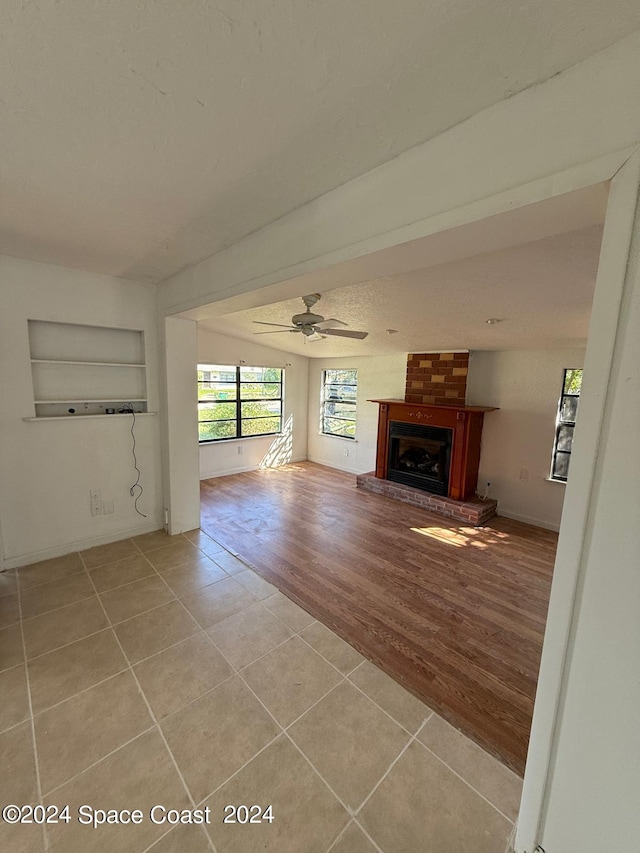 unfurnished living room featuring a brick fireplace, light hardwood / wood-style floors, and ceiling fan